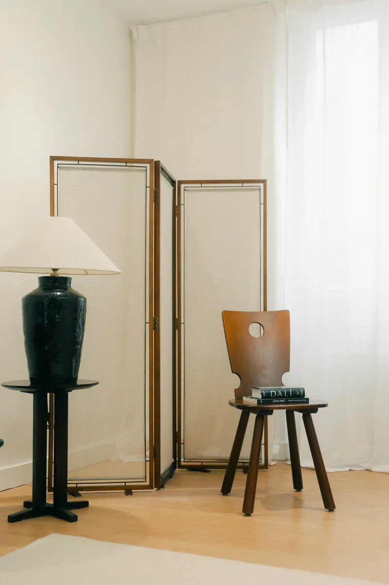 Chaise en bois, lampe à abat-jour et paravent doré dans une pièce claire.