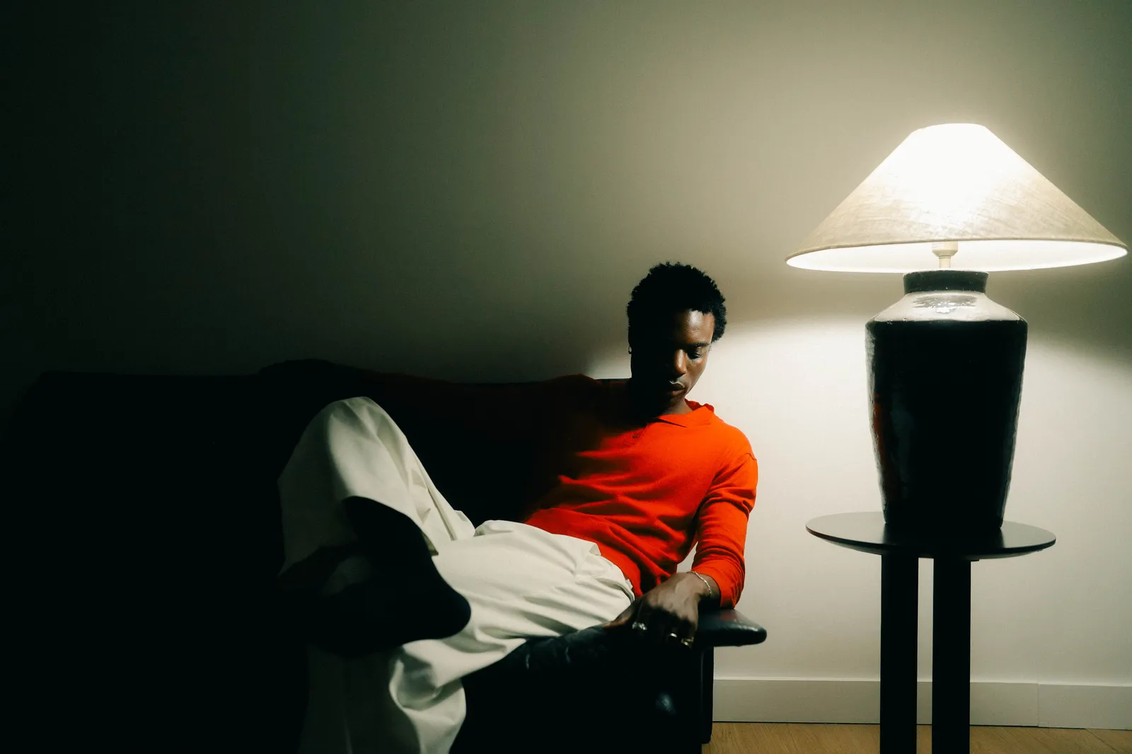 Personne allongée sur un canapé sombre, sous une lampe à abat-jour, en pull orange.