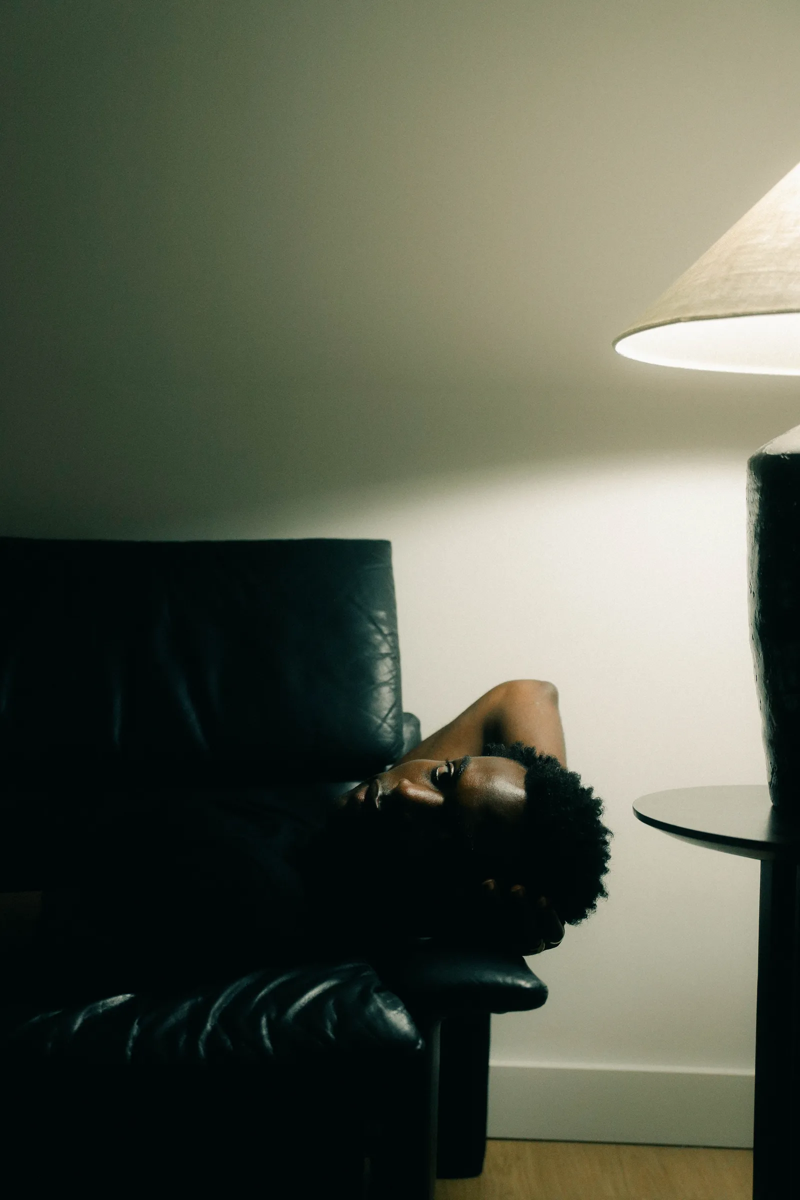 Personne allongée dans un fauteuil en cuir noir, sous une lampe à abat-jour.