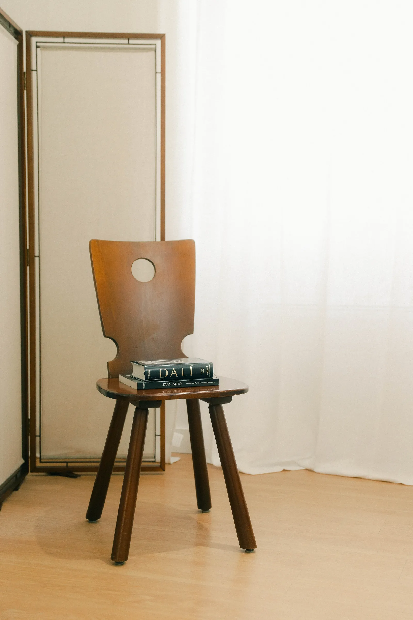 Chaise en bois au dossier ajouré, devant un paravent et un rideau de lin clair.